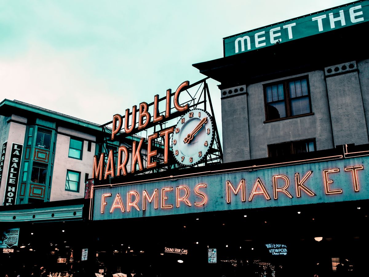 The image shows the entrance of a public market with a large neon "Farmers Market" sign and clock, likely a famous market in an urban area.